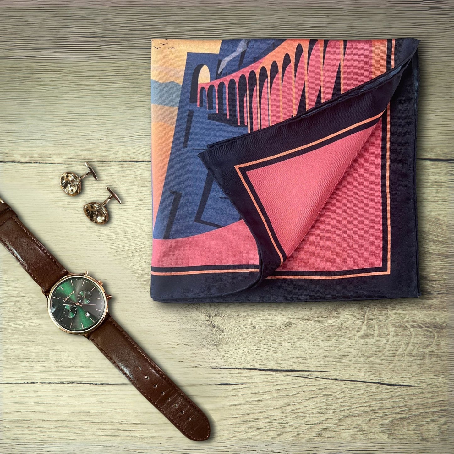 L'Odysee Pocket Square with scenic design on a wooden surface paired with a leather watch and bronze cufflinks