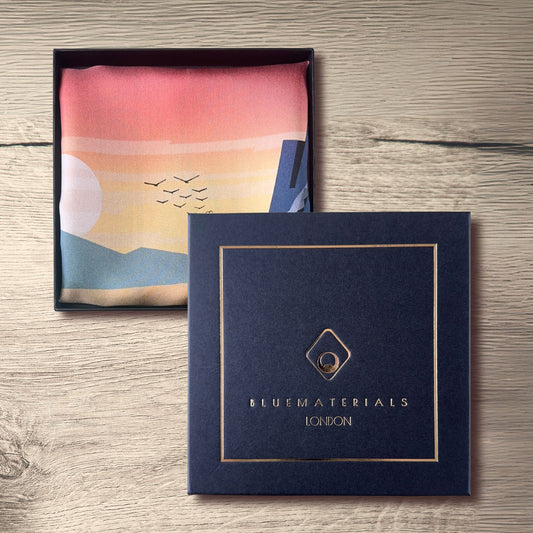 L'Odysee Pocket Square with a scenic design in a BLUEMATERIALS London luxury packaging on a wooden surface