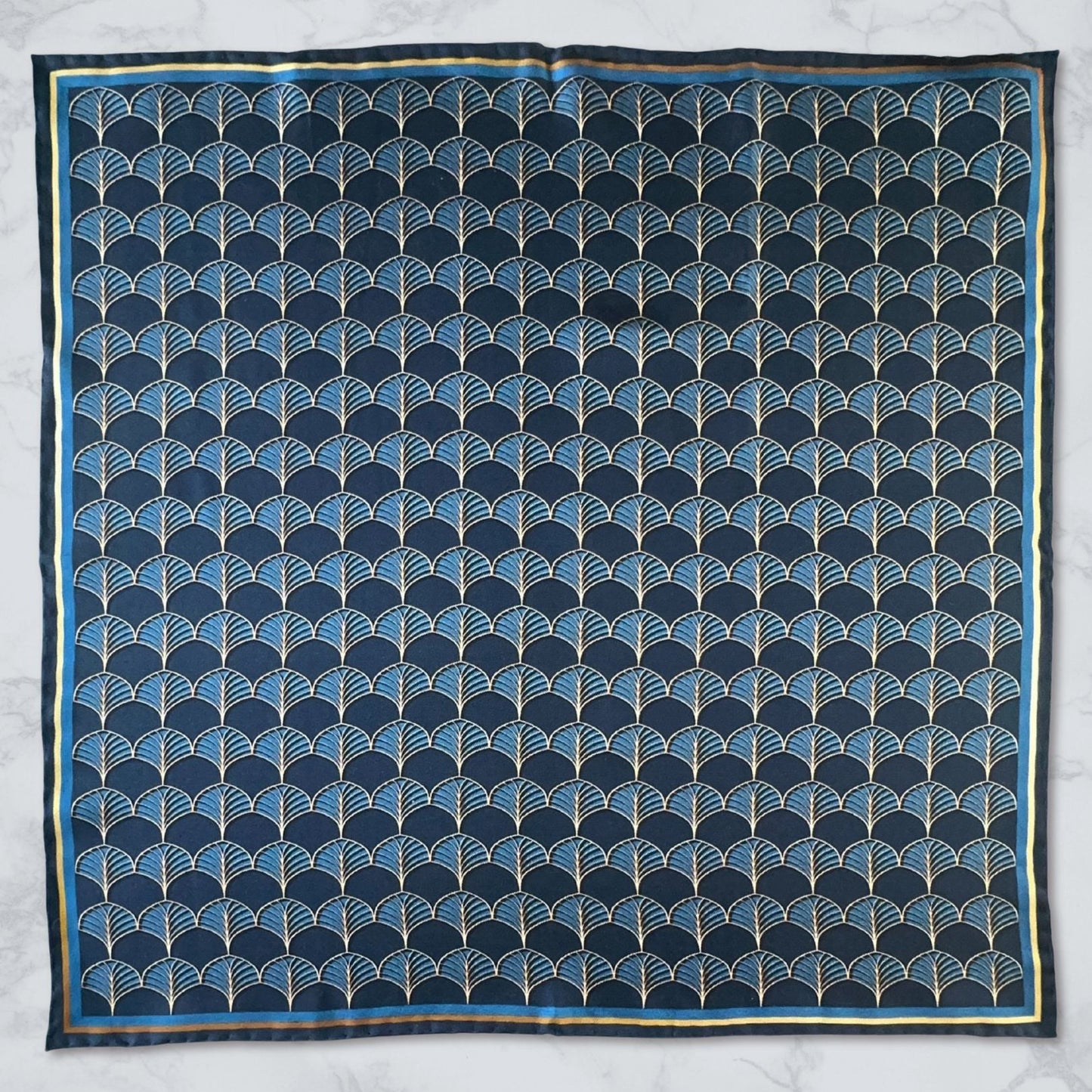 BLUEMATERIALS Midnight blue & gold silk pocket square, with a fan pattern inspired by art deco motifs, laid flat on a marble background.