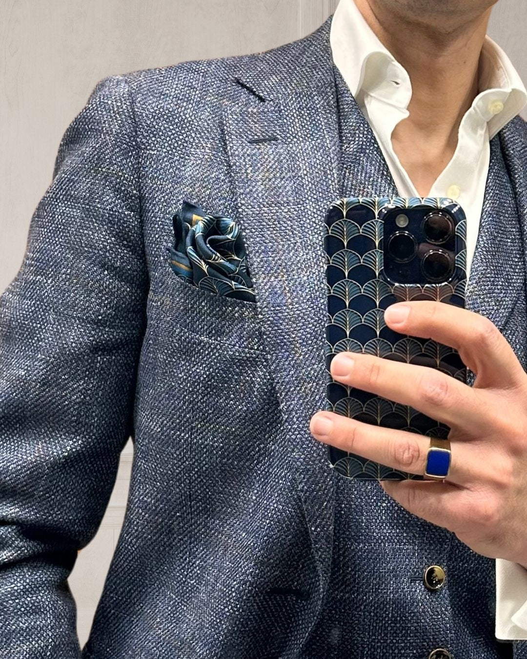 Midnight blue and gold pocket square in a twist-fold in a lapel pocket in a mirror view with matching phone case held by a hand wearing a gold ring with blue stone