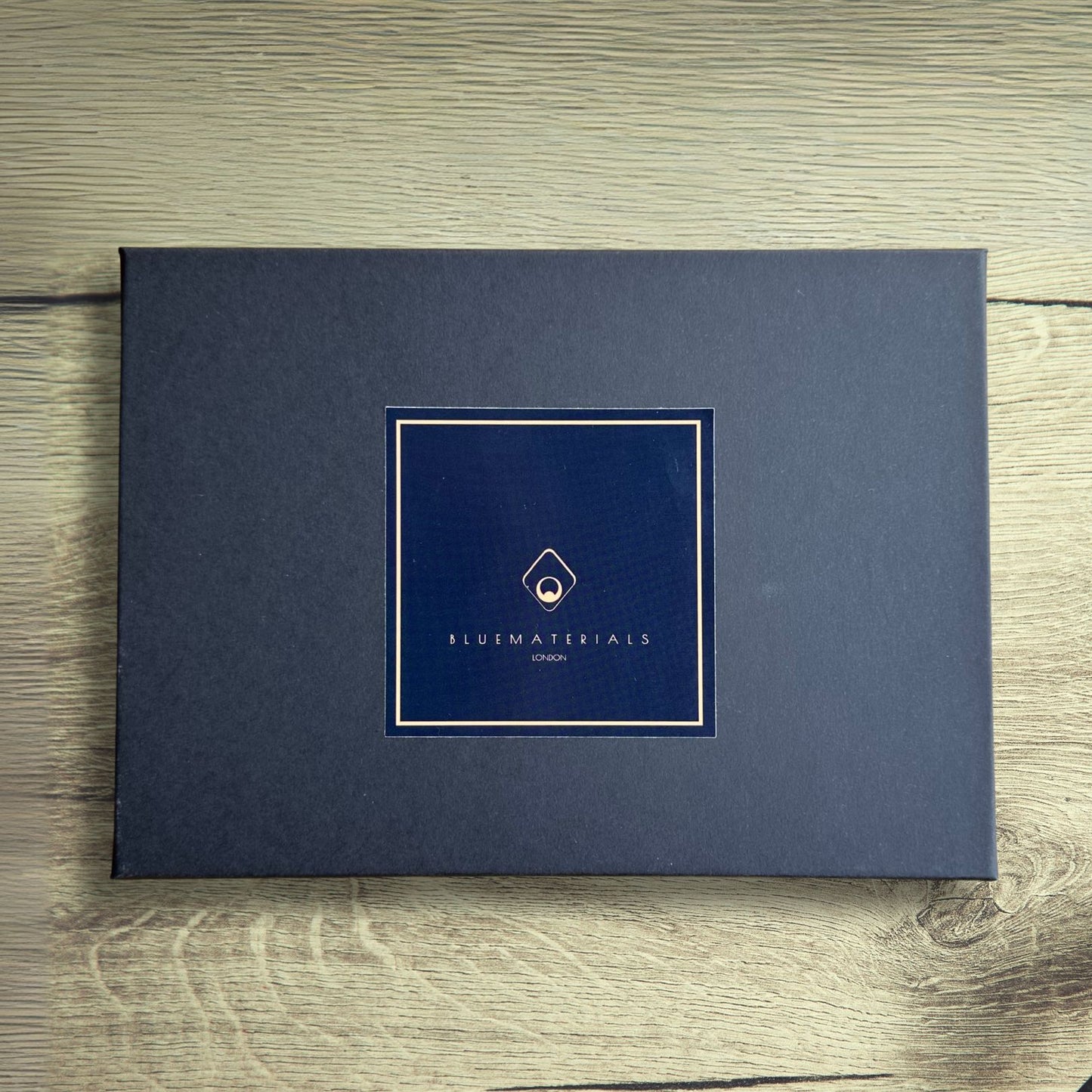 Dark grey gift box with BLUEMATERIALS branding and logo on a wooden rustic table