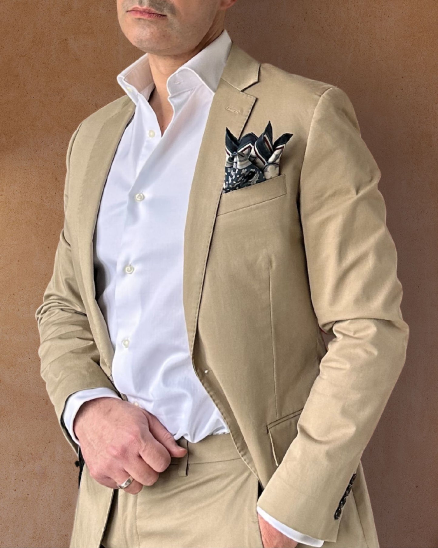 Blue cream and burgundy pocket square on the lapel pocket of a cream suit paired with a crisp white shirt on a tobacco background