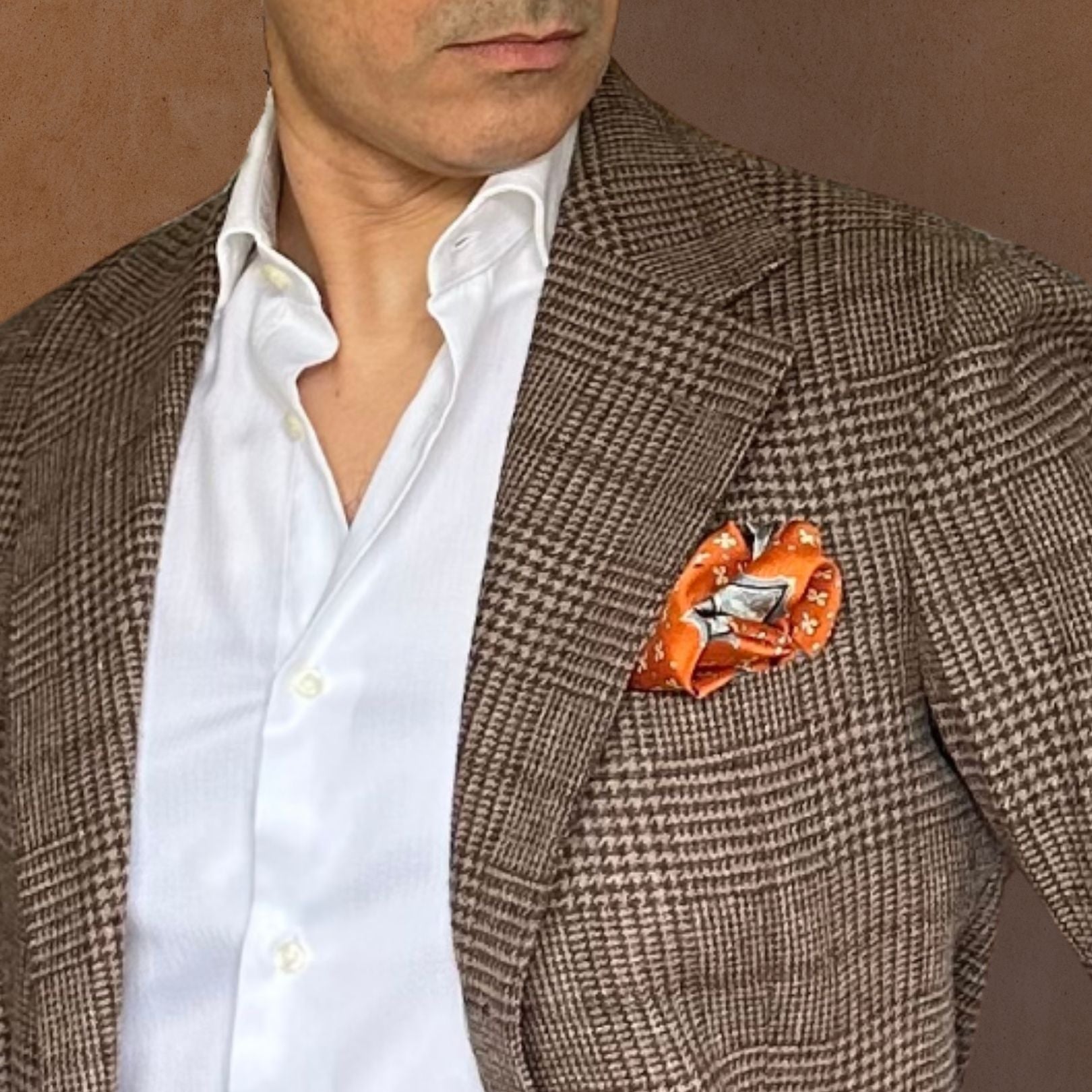 Man wearing a brown checkered blazer with an orange pocket square against a brown background
