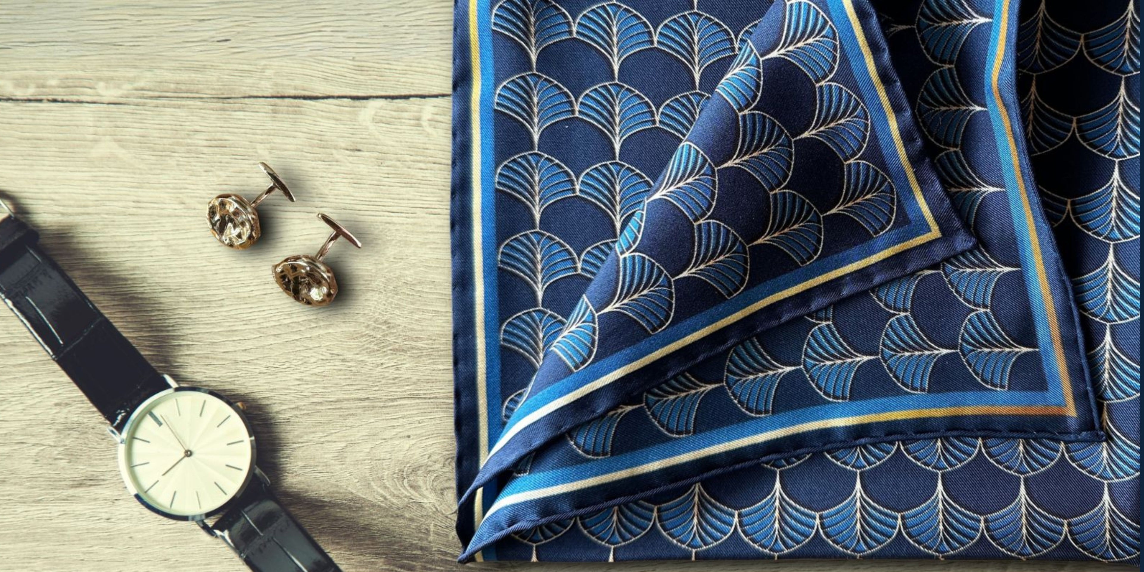 Blue patterned pocket square with cufflinks and watch on a wooden surface