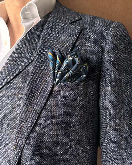 Midnight-blue pocket square in a peak-fold in the lapel pocket of a blue-grey textured suit jacket 