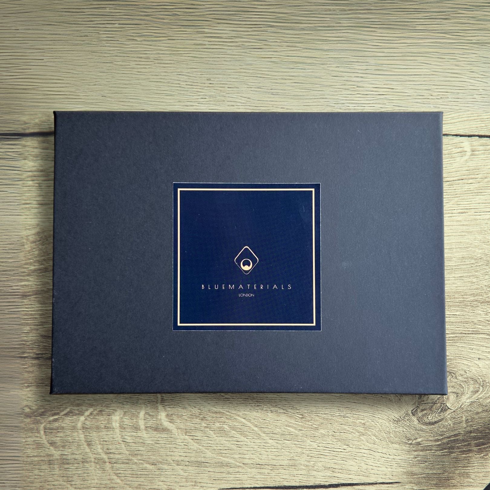 Dark grey gift box with BLUEMATERIALS branding and logo on a wooden rustic table 