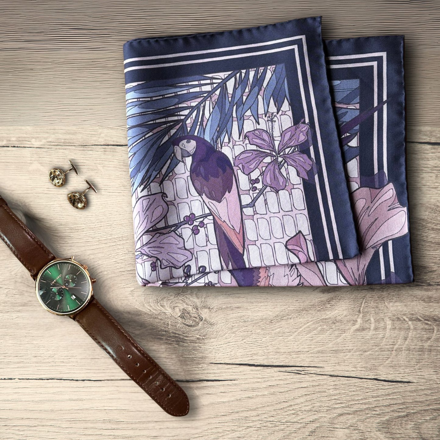 Pink purple, and navy blue pocket square folded on a rustic wooden table next to a brown leather watch and bronze cufflinks 