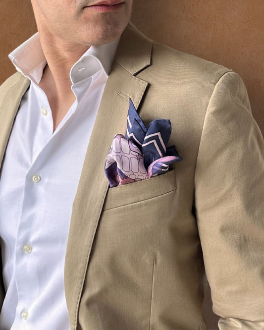 Pink and navy blue pocket square with peak fold on a lapel pocket of a cream jacket paired with a white shirt on a tobacco background