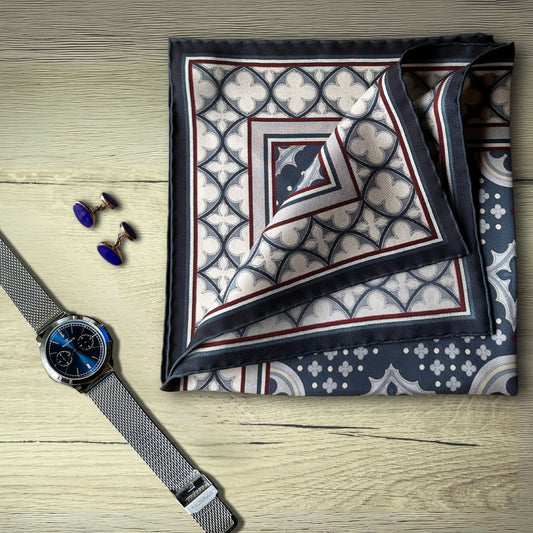 Blue cream and burgundy pocket square folded on a wooden rustic table next to a silver watch with a shimering blue face and two silver cufflinks with deep blue stones